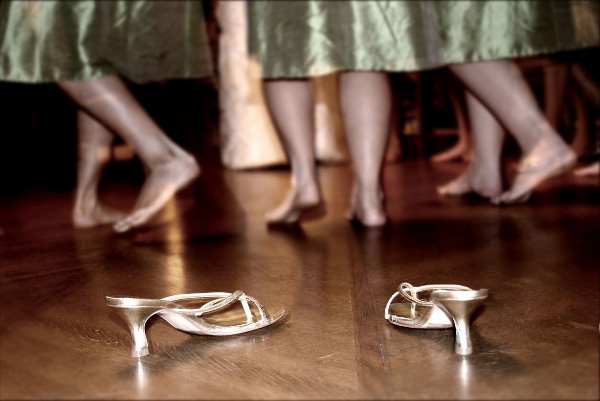 Three bridesmaids kick off their shoes to dance at a wedding reception